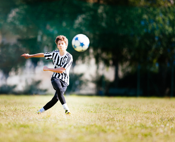 Poika pelaa jalkapalloa jalkapallokentällä.
 - Valokuva, kuva