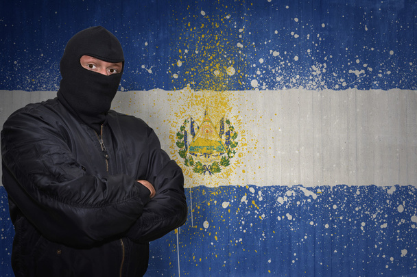 dangerous man in a mask standing near a wall with painted national flag of el salvador - Photo, Image