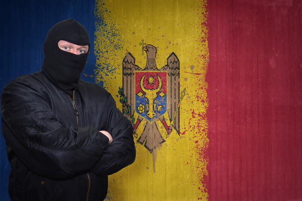 Gefährlicher Mann in Maske, der in der Nähe einer Mauer mit gemalter moldawischer Nationalflagge steht - Foto, Bild