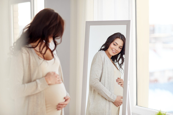 happy pregnant woman looking to mirror at home - Foto, Imagem