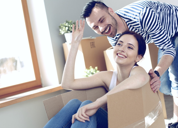 Happy couple having fun and riding in cardboard boxes at new home - Foto, imagen