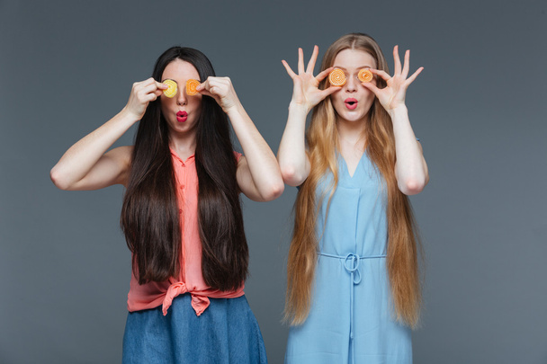 Two funny amazed women covered their eyes with marmalade candies  - 写真・画像