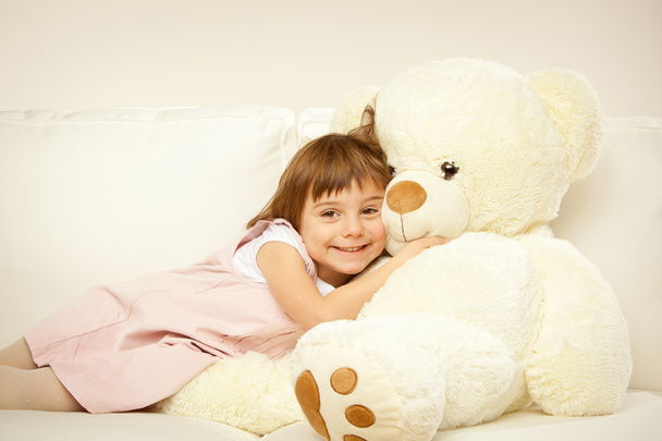 blonde female child play with her white teddy bear in a bed - Foto, Imagem