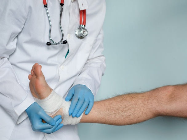 Nahaufnahme eines Arztes, der nach einem Unfall einen verletzten Fuß bandagiert - Foto, Bild