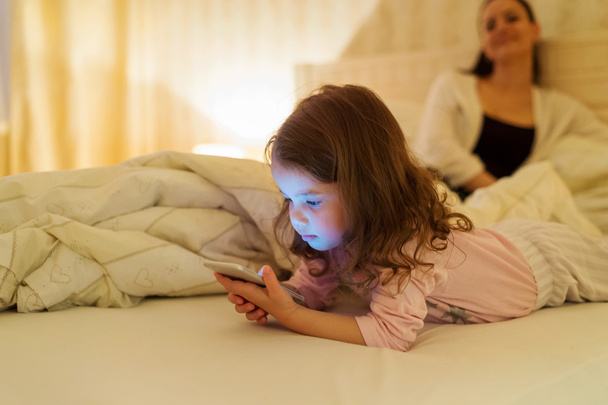 Little girl with smartphone lying in a bed, bedtime - Valokuva, kuva