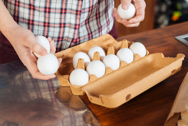Fresh eggs holded by hands of young woman on kitchen - 写真・画像