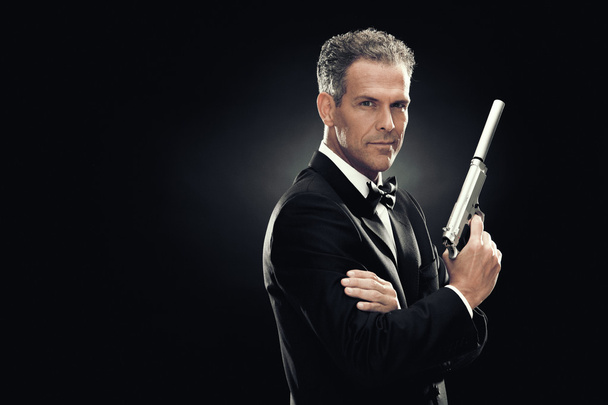 elegant man with bow tie and gun isolated on black - 写真・画像