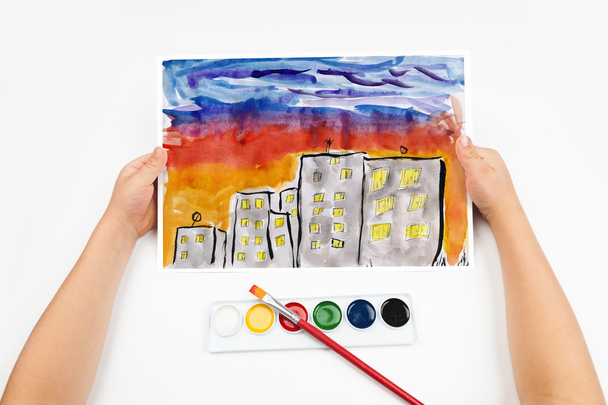 kaupungin siluetti auringonlaskun aikaan, pilvenpiirtäjä valolla ikkunassa, kodin siluetti tummalla taustalla, lasten piirustus, ylhäältä näkyvä kädet lyijykynällä maalaus kuva paperilla, taideteos työpaikalla
 - Valokuva, kuva