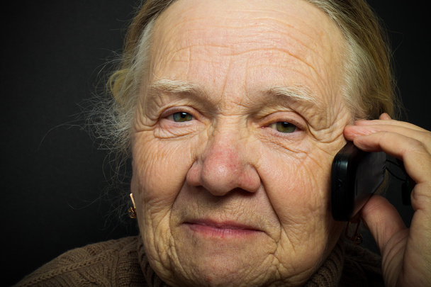Porträt einer älteren Frau mit Telefon auf dunklem Hintergrund. Tonne - Foto, Bild