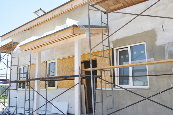 Construction de la maison rurale avec avant-toit, fenêtres, porte, façade de fixation, isolation, plâtrage et peinture mur de la maison extérieure
.  - Photo, image