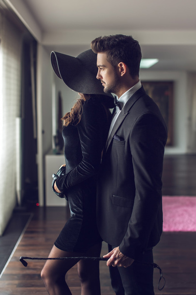 Sexy macho man in tuxedo holding whip and lover - Photo, Image