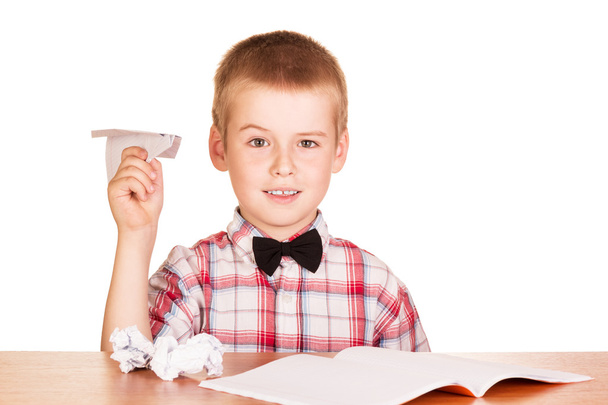 Αγόρι κάθεται στο τραπέζι και κάνει αεροπλάνα χαρτί απομονωθεί. - Φωτογραφία, εικόνα