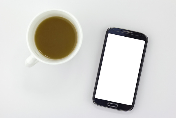 白で隔離のコーヒー カップの横に座っている空白の画面を持つスマート フォン - 写真・画像
