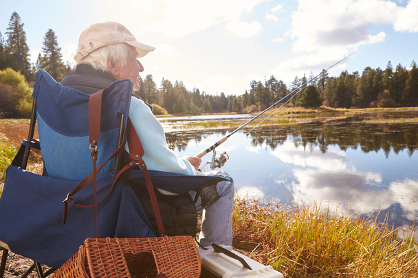 Senior man sits fishing in a lake - Foto, imagen
