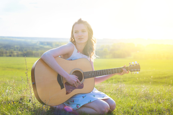 Country  girl sitting with acoustic guitar at field  - Fotoğraf, Görsel