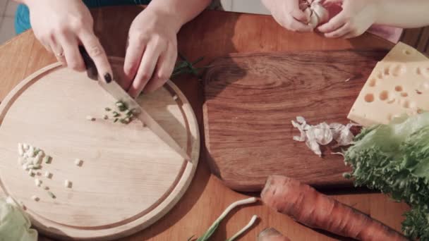 Madre e hija cortando cebolla y ajo sobre tabla de madera
 - Metraje, vídeo