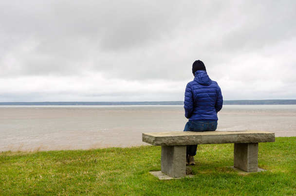 Μοναχική γυναίκα που κάθεται σε ένα παγκάκι, μπροστά στη θάλασσα - Φωτογραφία, εικόνα