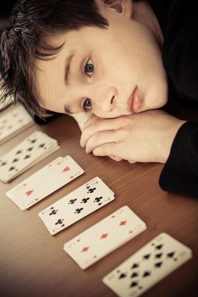 Smutny chłopiec kładzie głowę na stole przez wiersz kart - Zdjęcie, obraz