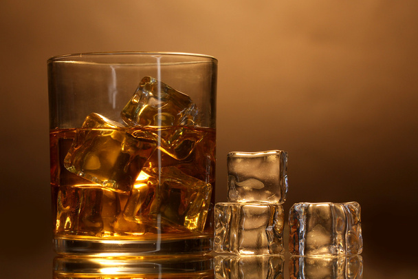 Glass of whiskey and ice on brown background - Foto, imagen