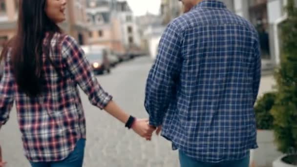 Romantische jongeren en liefde, man en vrouw als mannelijke en vrouwelijke studenten lopen en hand in hand in stadspark. Tilt shot, slow-motion - Video