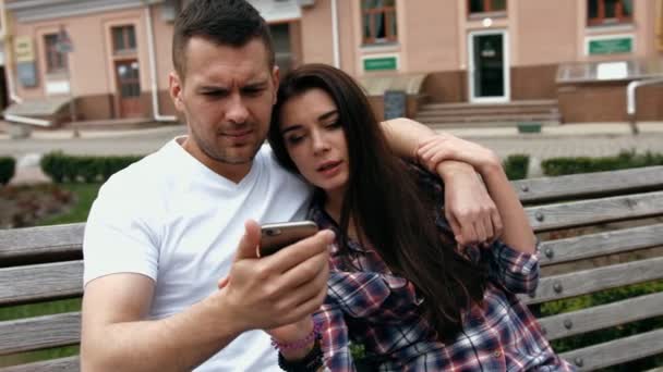 Joven urbano hombre vistiendo camiseta blanca y mujer con camisa a cuadros con teléfonos sentados en un banco
 - Imágenes, Vídeo