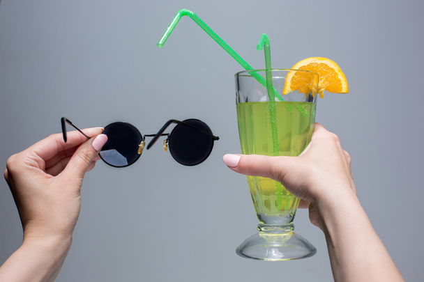 The female hands with cocktail and sunglasses on gray background - Foto, immagini
