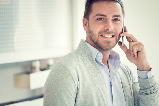 smiling young casual businessman talking on the phone at office - Foto, afbeelding