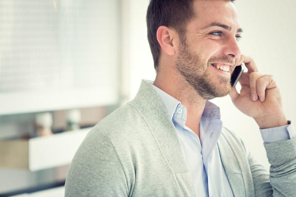 smiling young casual businessman talking on the phone at office - 写真・画像