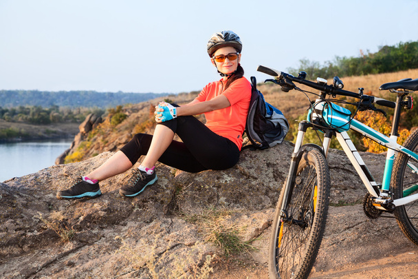 Aikuinen viehättävä naispyöräilijä istuu kivellä ja lepää
. - Valokuva, kuva
