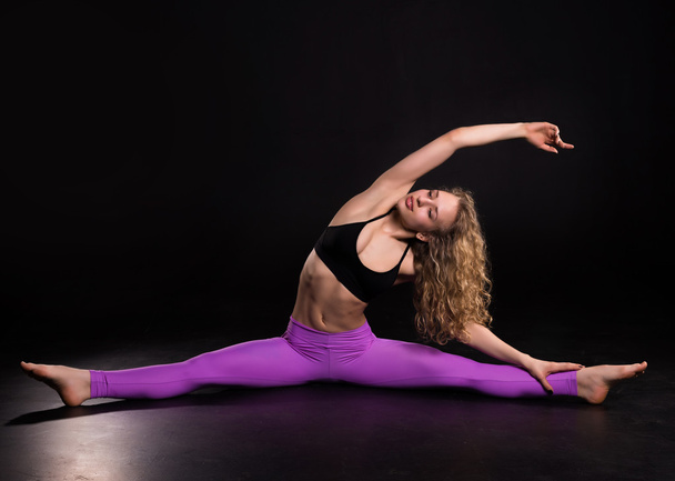 Fitness woman training in dark studio. Young girl stretching - Zdjęcie, obraz