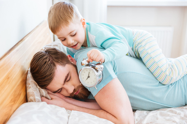 Little son holding alarm clock near sleeping father ear - Foto, Imagen