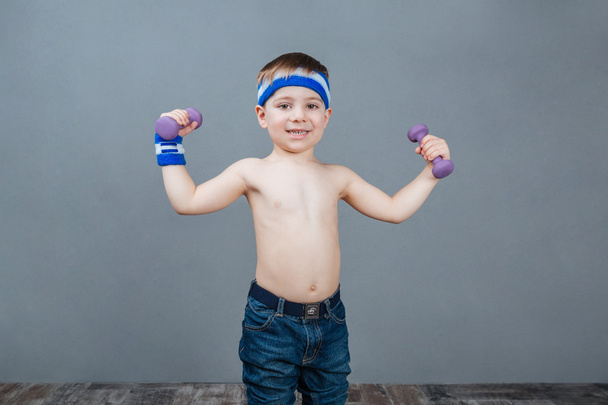 Happy cute little boy standing and doing exercises with dumbbells - Photo, image
