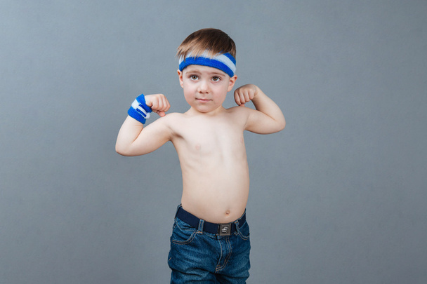 Portrait of shirtless little boy standing and showing biceps - Fotó, kép