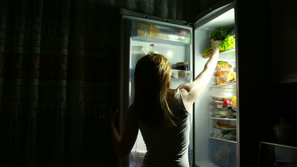 Woman opens the refrigerator at night. night hunger. diet. eating sandwich - Footage, Video