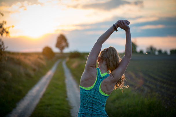 Happy successful sportswoman raising arms to the sky on golden back lighting sunset summer. Fitness athlete with arms up celebrating goals after sport exercising and working out outdoors.  - Photo, Image