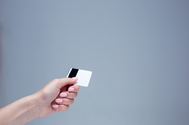 The card in a female hand is on a gray background - Фото, изображение