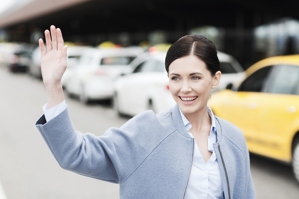 smiling young woman with waving hand over taxi - Fotó, kép