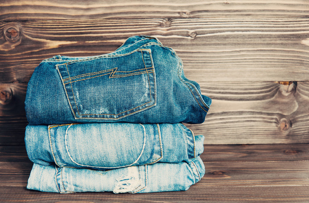jeans stacked on a wooden background, vintage toned - Photo, Image