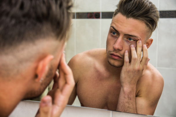 Young man touching his face while looking in mirror - Fotografie, Obrázek