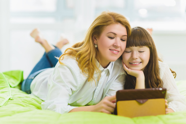 happy family. Mother and daughter sitting on the bed with a tablet - Foto, Imagem