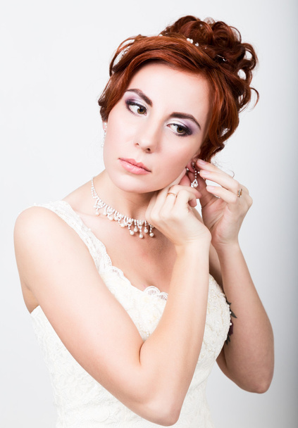 beautiful bride in a wedding dress with a wedding makeup and hairstyle. Bride inserts earrings in her ear - Valokuva, kuva