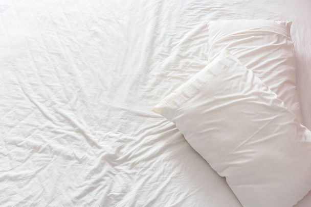 Bovenaanzicht van een onopgeruimd/ongemaakt bed met witte verfrommeld Laken en twee rommelig kussens in een hotelkamer. - Foto, afbeelding