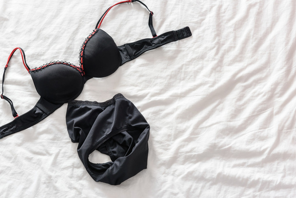 Weergave van vrouw zwarte beha top / lingerie dat is opgestegen en zetten een rommelig onopgemaakte bed. - Foto, afbeelding