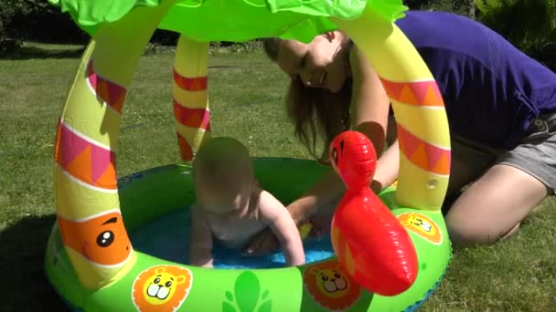 baby girl swim in rubber water pool in park. Mother keep child. 4K - Footage, Video