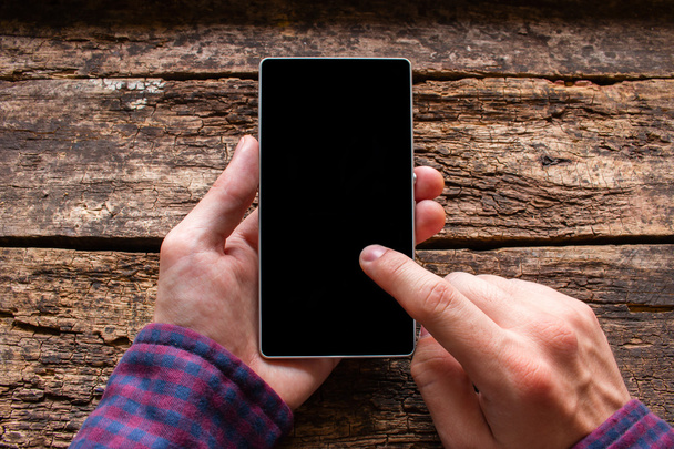 man touches the screen in the phone on a wooden background mockup - Photo, Image