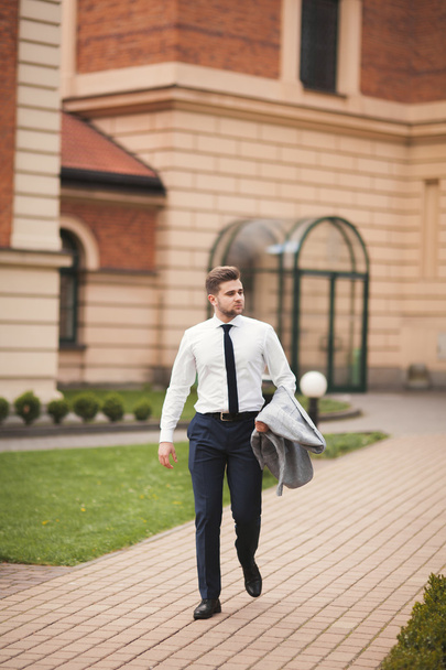 Stylish businessman walking outdoors and looking away - 写真・画像