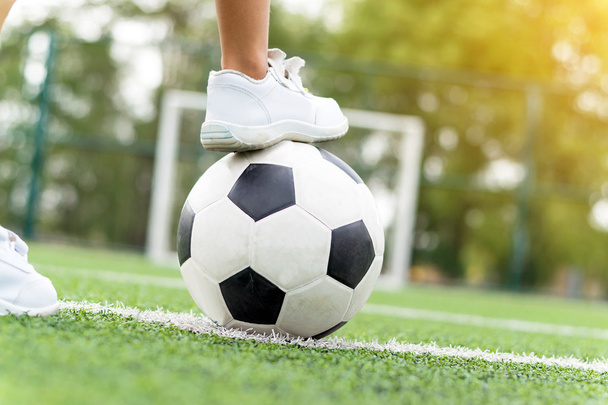 Feet of a boy wearing white sneakers stepping on a soccer ball. - 写真・画像