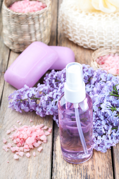 Spa background with blossoming lilac flowers and bottle of essential oil or flower hydrolat, cosmetic aroma soap and  sea salt - Photo, Image