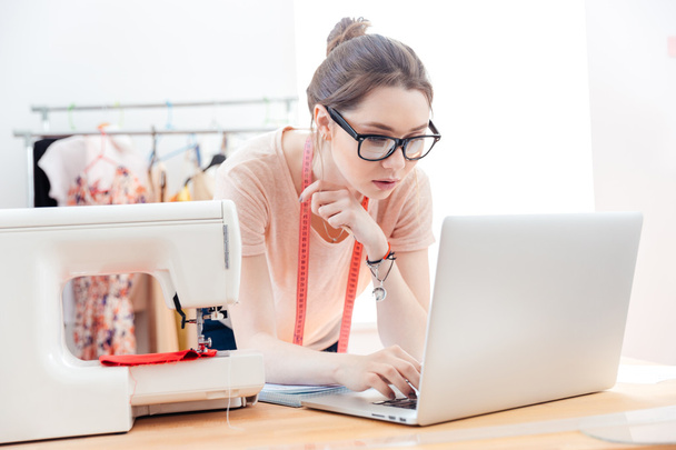 Serious woman seamstress using laptop in studio - Фото, изображение