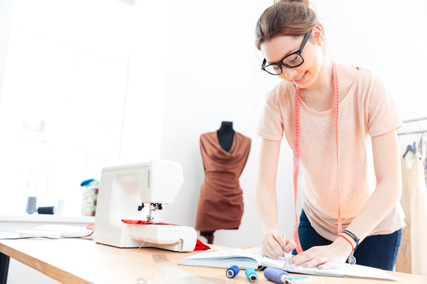 Happy woman seamstress wearing glasses standing and drawing in workshop - Photo, Image